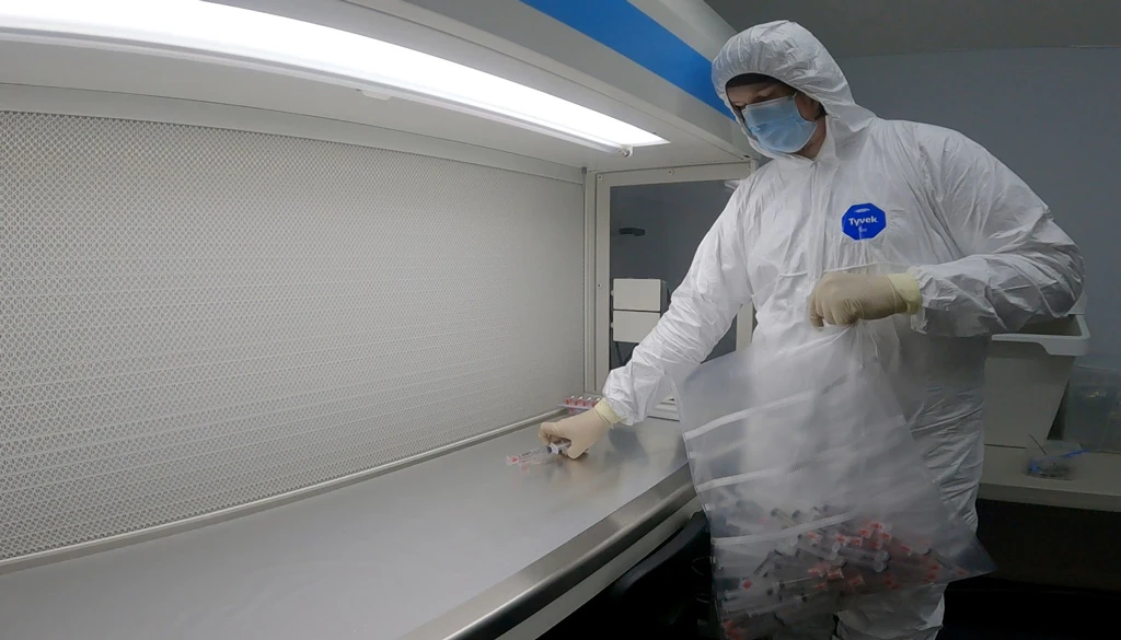 cleanroom worker wearing a tyvek suit preparing and packaging products infront a flowhood